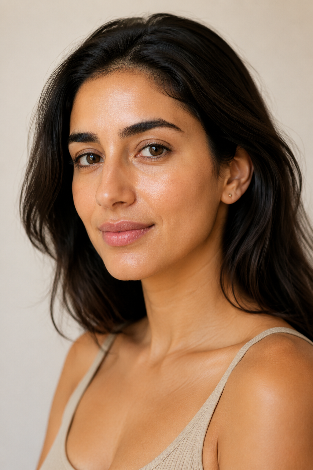 Editorial portrait of a woman with warm medium skin tone and dark hair, shown in soft natural light on a warm neutral backdrop